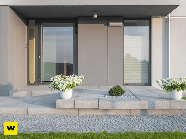 Moderner Hauseingang mit großen Glasfronten, Steinplatten und weißen Blumenkübeln.